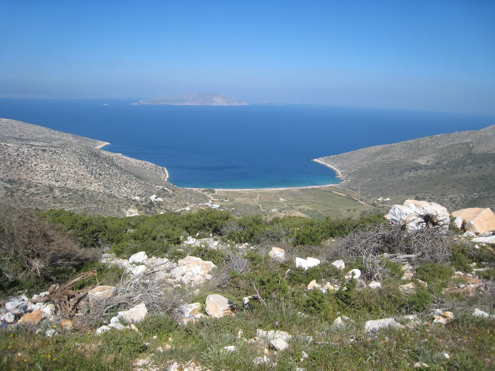 סמטה לבנה בכפר חורה באיוס ביוון עם מדרגות אבן כנסייה כחולה ופרחים סגולים