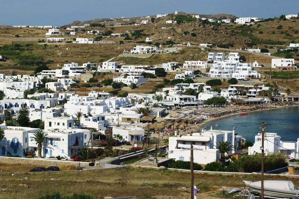 סמטה לבנה ומפותלת עם בוגנוויליה סגולה ותריסים צבעוניים בעיר חורה במיקונוס, יוון